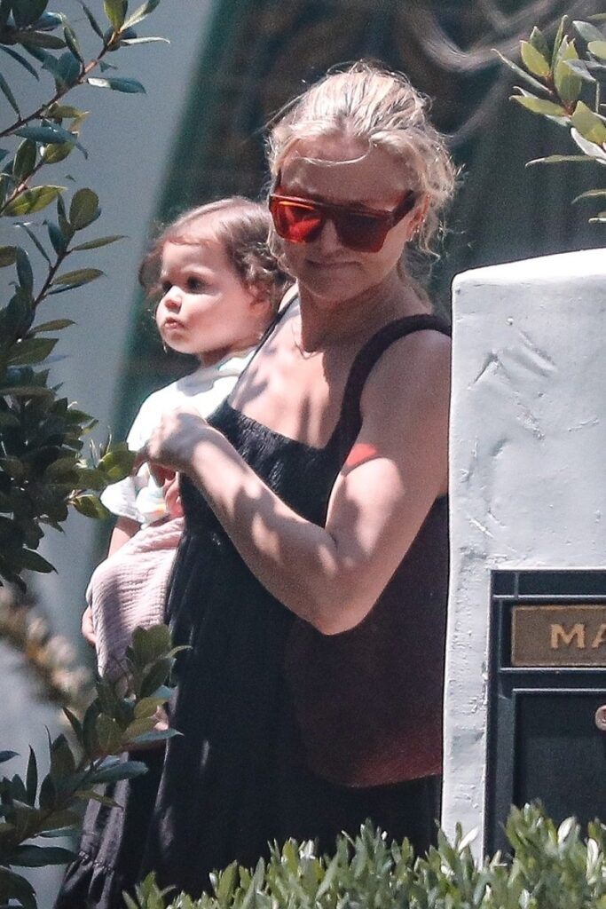 Cameron Diaz și fiica ei, Raddix, în Beverly Hills, California. Ea îmbrăcată într-o rochie neagră, lejeră, fetița imbrăcată în alb, fundal cu verdeață