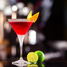 Un pahar pe un bar care este umplut cu un coktail cosmopolitan și decorat cu o felie de coajă de portocală