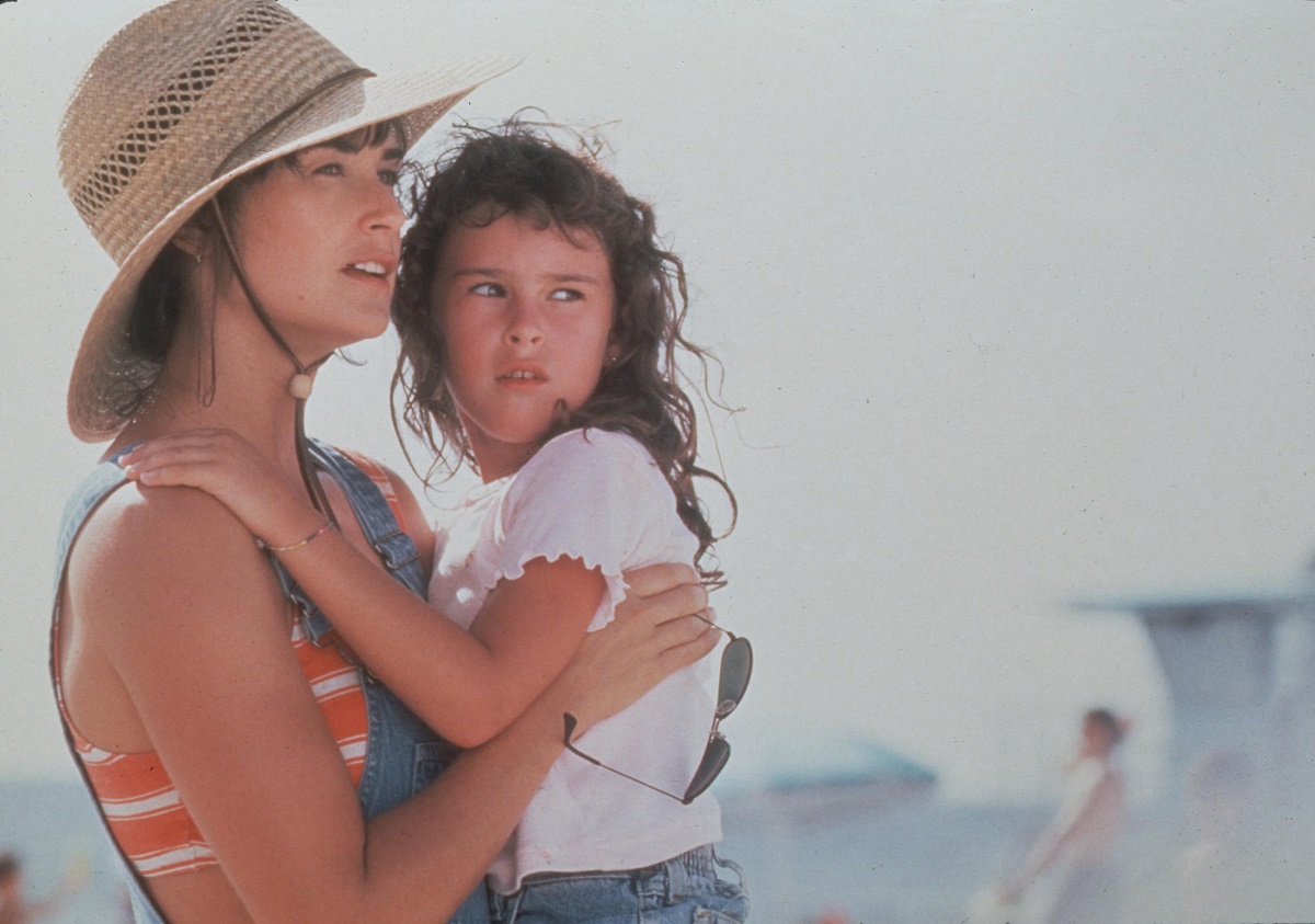 Demi Moore și fiica ei, Rumer Willis, în filmul Striptease. Ea poartă pălărie de paie, bluză în dungi cu galben și verde, salopetă de blugi. Rumer poartă salopetă de blugi și bluză albă, fundal cu cer