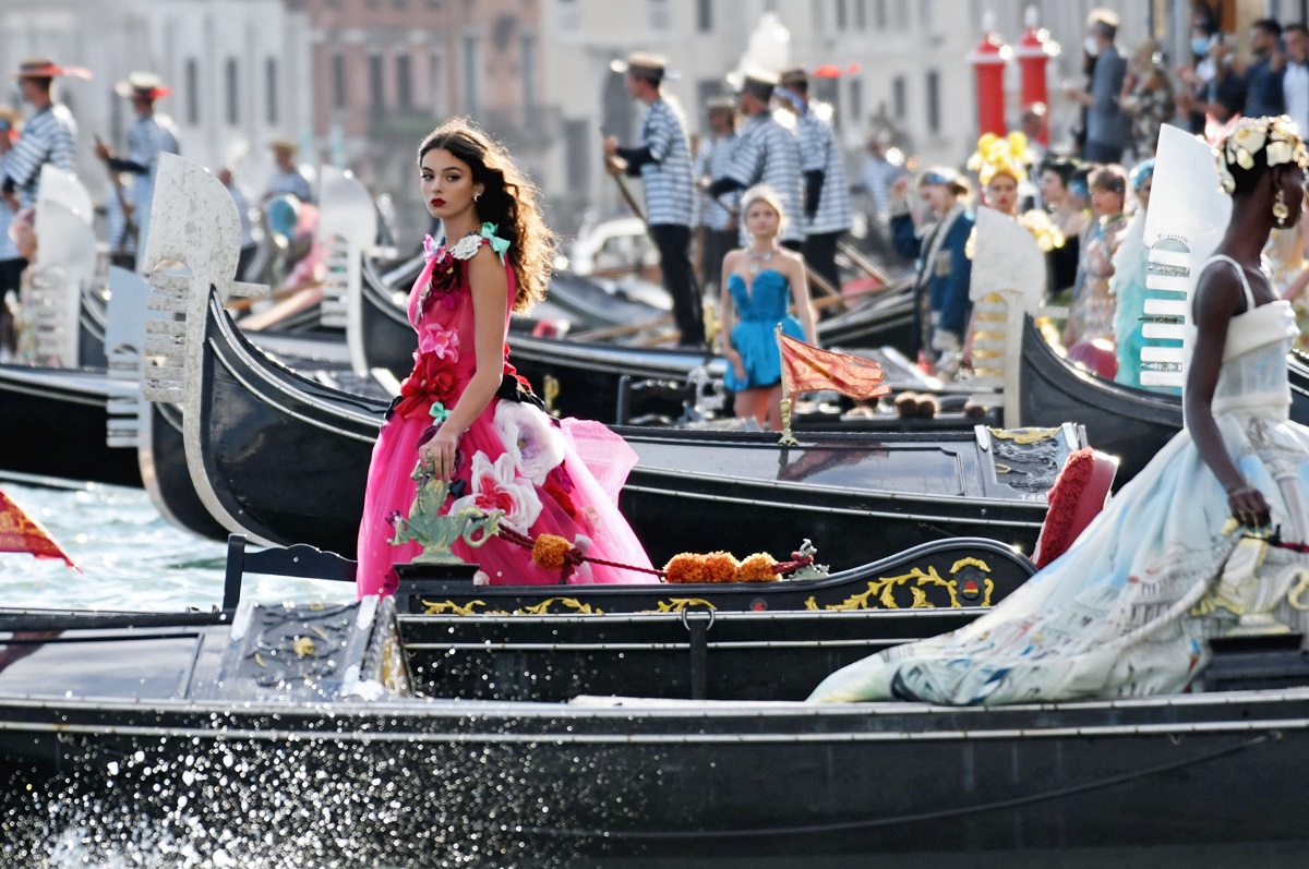 Deva Cassel, fiica Monicăi Bellucci cu Vincent Cassel, la prezentarea de modă Dolce & Gabbana Alto Moda, Veneția, august 2021. Ea poartă o rochie magenta, cu aplicații. E în gondolă. Pe fundal se văd apă și bărci