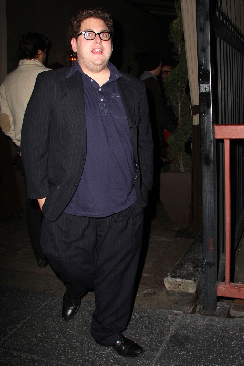 Jonah Hill surprins de paparazzi în West Hollywood, în anul 2008. Îmbrăcat în costu negru, cămașă albastru închis, fundal cu stradă