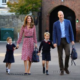 Kate Middleton și Prințul William au mers împreună cu Prințul George și Prințesa Charlotte în prima zi de școală a Prințesei, în anul 2019. Copiii poartă uniforma neagră, Kate are o rochie roșie cu al, și William poartă o bluză albastră