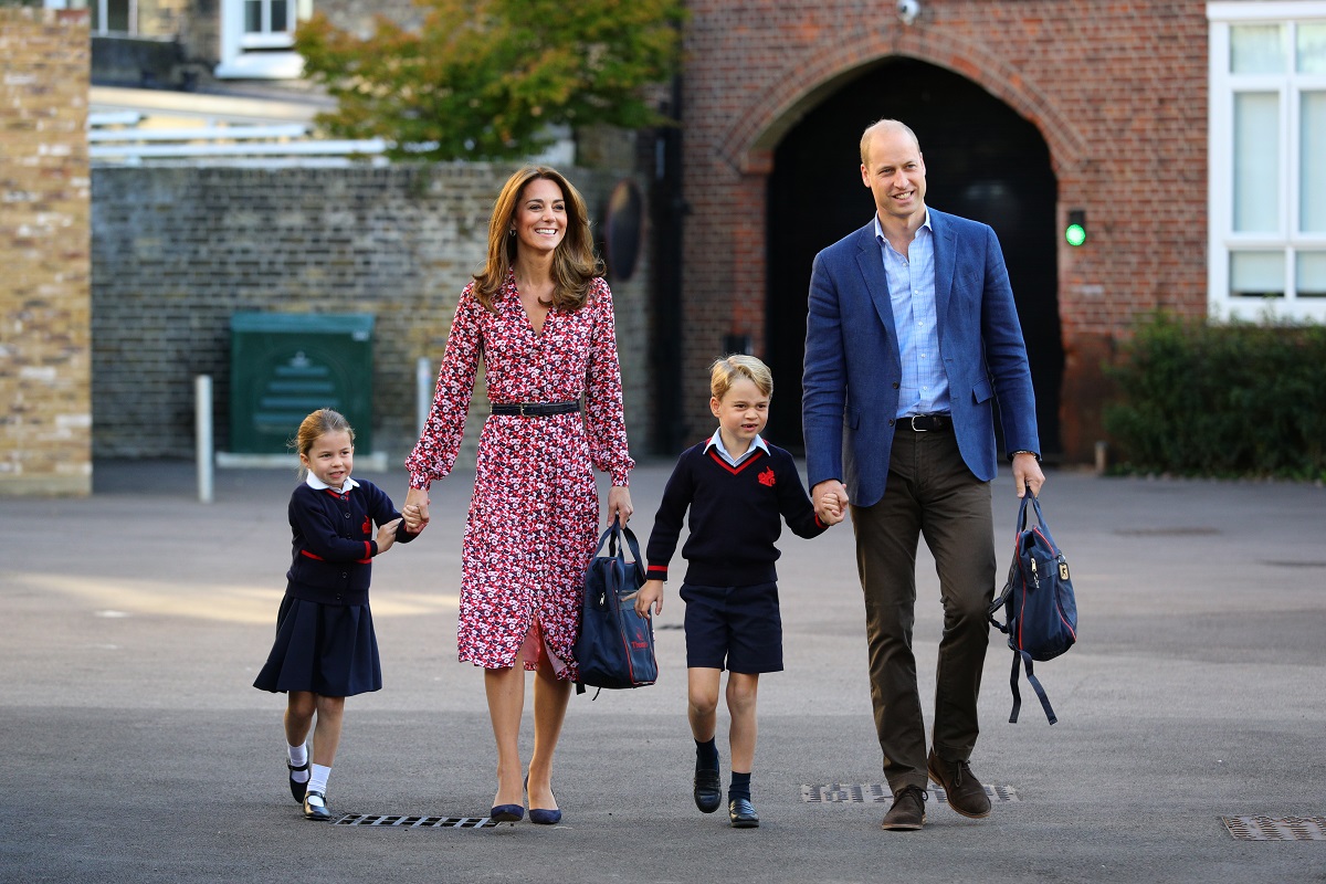 Kate Middleton și Prințul William au mers împreună cu Prințul George și Prințesa Charlotte în prima zi de școală a Prințesei, în anul 2019. Copiii poartă uniforma neagră, Kate are o rochie roșie cu al, și William poartă o bluză albastră