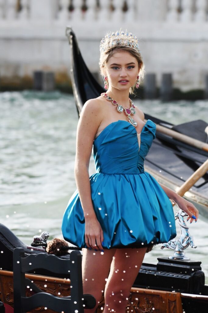 Leni Klum, fiica lui Heidi Klum, la prezentarea de modă Dolce & Gabbana Alto Moda, din Veneția, august 2021. Ea a purtat o rochie albastră, cu corset, scurtă și cu decolteu. A accerosizat-o cu o coroană și diamante colier. Pe gondolă, cu fundal cu apă și bărci