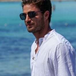 Maxi Iglesias, cu ochelari de soare, într-o cămașă albă, la plajă, în timpul unei ședințe foto