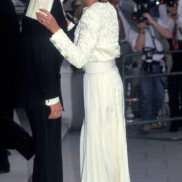 Prințesa Diana și-a asortat rochia albă cu geanta plic, de aceeași culoare. În imagine, ea poartă o rochie albă, lungă, cu măneci lungi, un plic alb și sărută pe obraz un bărbat îmbrăcat în costum negru