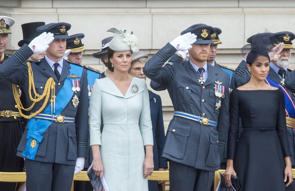 Prințul William, Kate Middleton, Prințul Harry, Meghan Markle au participat împreună la ceremonia RAF 100, de la Buckingham Palace, în anul 2018. Ei au purtat costumele lor albastre, Kate s-a îmbrăcat într-o ținută albastră, Meghan a purtat o ținută neagră