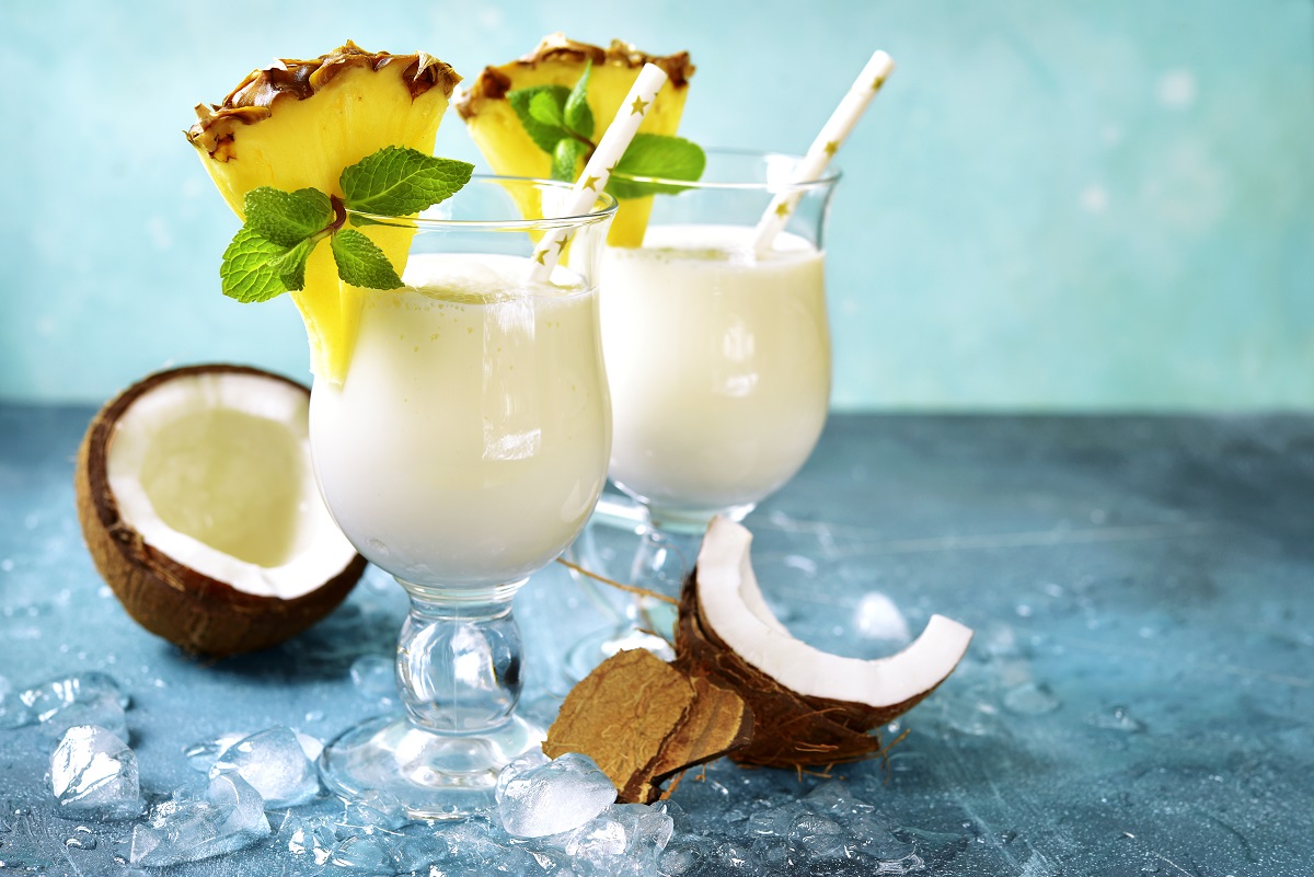 Două pahare pe un blat albastru umplute cu pina colada, un cocktail sofisticat fără alcool, și decorate cu felii de ananas