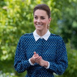 Kate Middleton și-a dezinfectat mâinile în cadrul unei vizite la spital în iulie 2020. Ea a purtat o rochie albastră, cu buline și guler albe. Pe fundal se vede verdeață