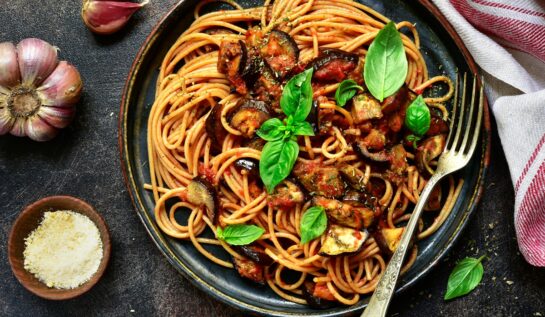 Spaghetti alla Norma într-o tigaie, alături de un bol cu brânză răzuită și usturoi