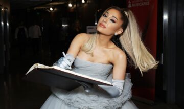 Ariana Grande într-o rochie gri în timp ce semnează un album și se află pe lista cu cele mai bogate vedete care au sub 30 de ani