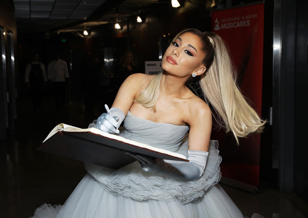 Ariana Grande într-o rochie gri în timp ce semnează un album și se află pe lista cu cele mai bogate vedete care au sub 30 de ani