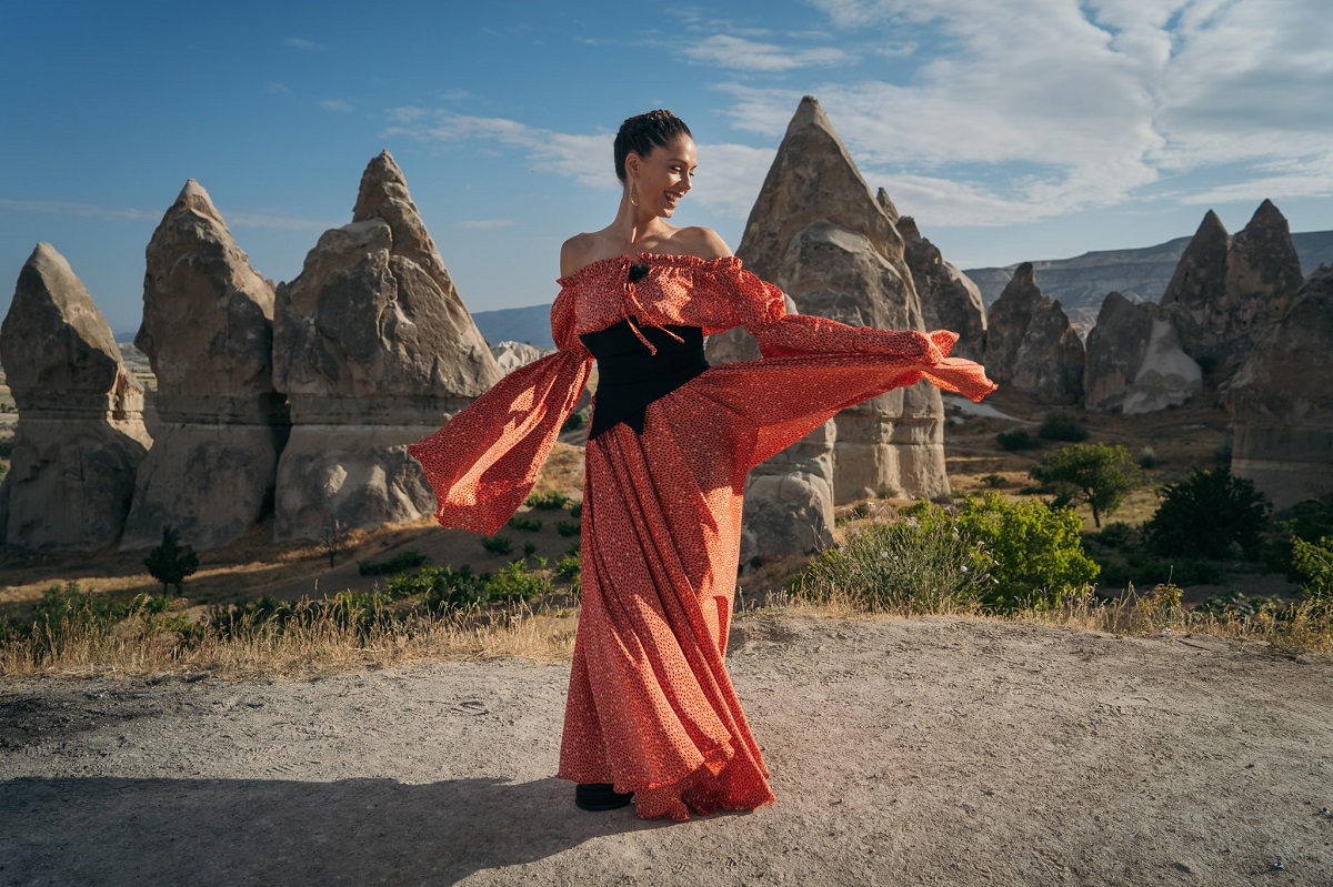Irina Fodor, prezentatoarea emisiunii Asia Express: Drumul Împăraților într-o rochie lungă portocalie pe un deal din Turcia