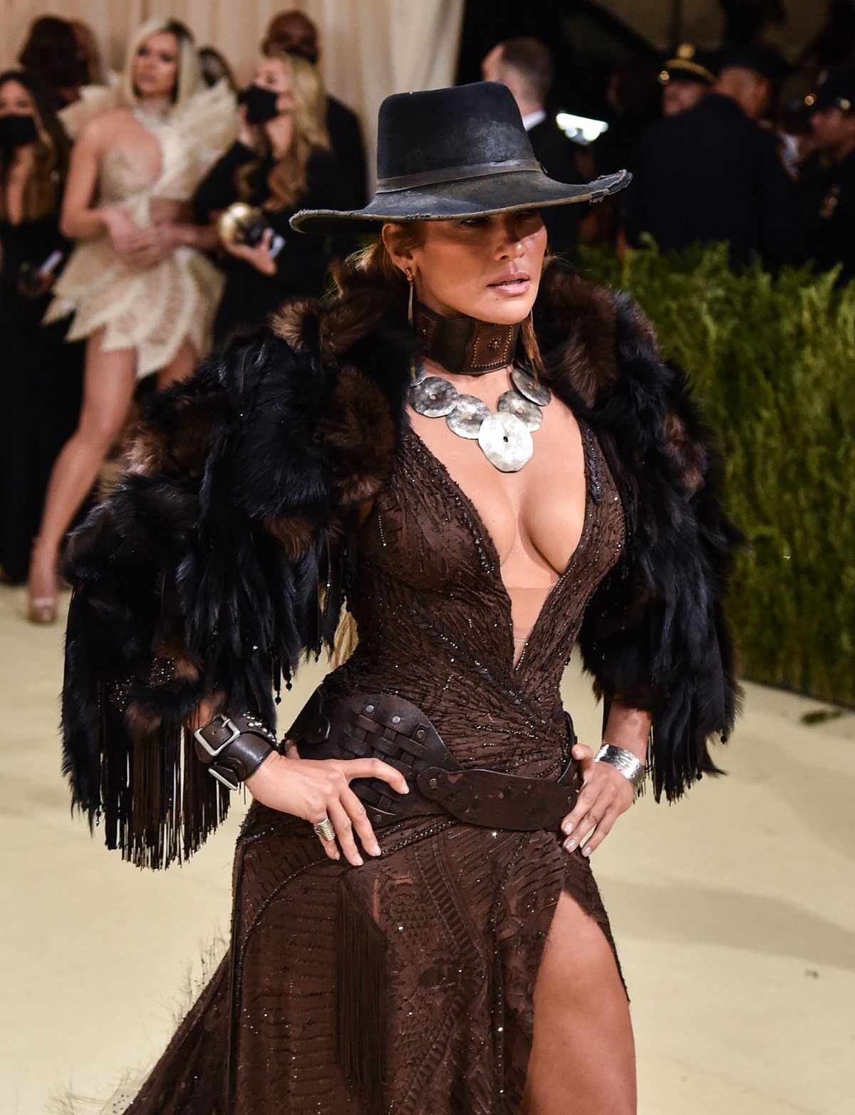 Jennifer Lopez într-o rochie mulată maro, peste care are o mantie cu pene și o pălărie de piele la Met Gala 2021