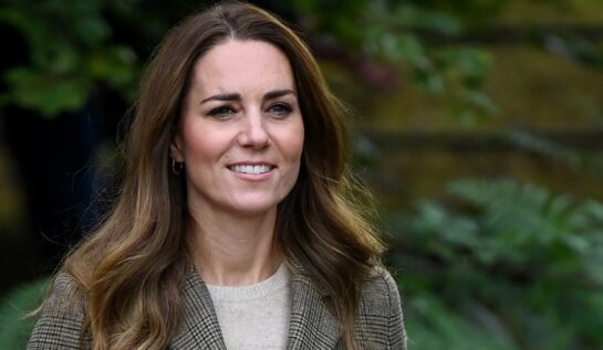 Kate Middleton zâmbind în timp ce poartă o bluză gri și un sacou în carouri