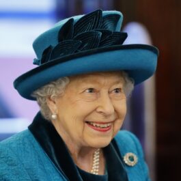 Portret al Reginei Elisabeta care poartă o pălărie albastră cu pene și un costum albastru în timp ce participă la o întâlnire oficială din anul 2019