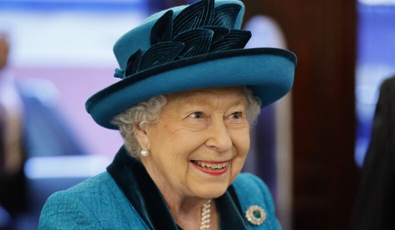 Portret al Reginei Elisabeta care poartă o pălărie albastră cu pene și un costum albastru în timp ce participă la o întâlnire oficială din anul 2019