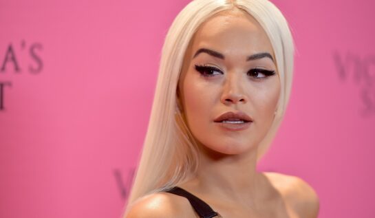 Portret al artistei Rita Ora cu părul lung blond dat pe spate în timp ce zâmbește la fotografi pentru evenimentul Victoria's Secret Fashion din 2018