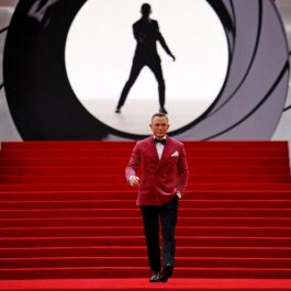 Daniel Craig într-un costum cu sacou roz în timp ce coboară scările acoperite de covorul roșu la premiera filmului James Bond No Time to Die