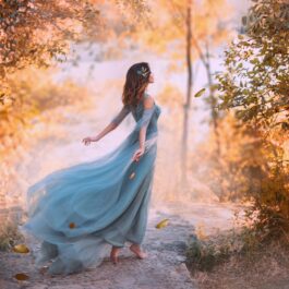 O femeie frumoasă care poartă o rochie albastră și privește în zare într-o pădure arămie de toamnă, fiind una din acele zodii care se fac remarcate toamna aceasta