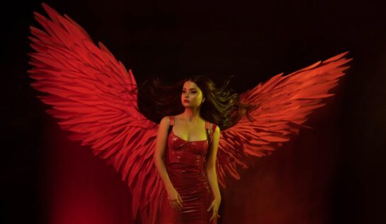 O femeie frumoasă îmbrăcată într-o rochie roșie care are în spate o pereche de aripi mari, roșii și reprezintă una din acele zodii extrem de geloase