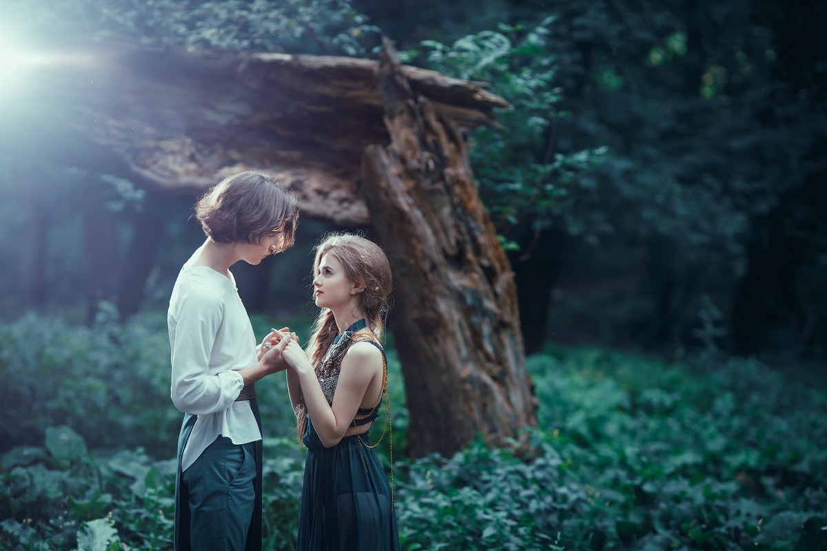 Un cuplu de îndrăgostiți într-o pădure în timp ce se țin de mâini și se privesc în ochi fiind zodii iubitoare