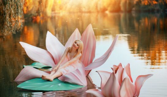 O femeie frumoasă care poartă o rochie roz și stă pe o floare de nufăr în mijlocul unui lac în timp ce reprezintă una din acele zodii norocoase în ziua de 29 septembrie 2021