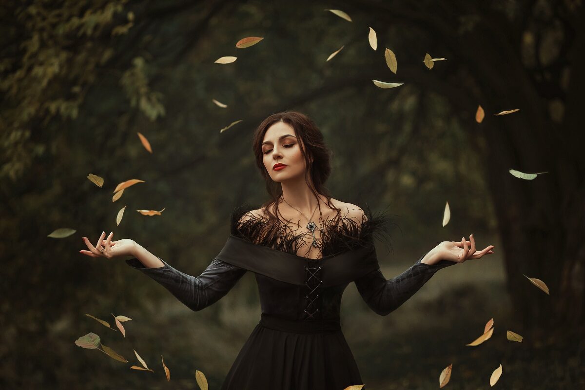 O femeie frumoasă îmbrăcată într-o rochie neagră în timp ce se află într-o pădure iar în jurul său plutesc în cerc frunzele copacilor pentru a potrtretiza una din acele zodii răzbunătoare