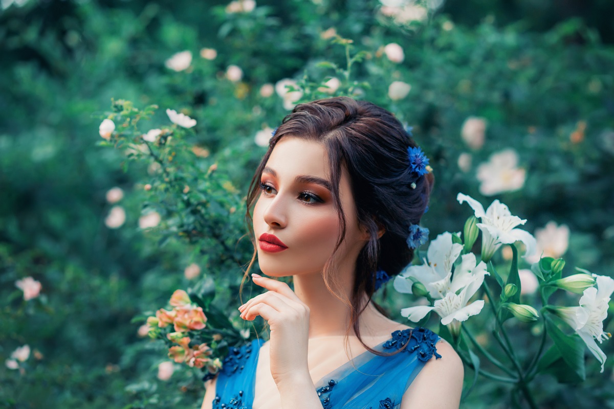 o femeie frumoasă cu părul prins care stă printre iarbă și flori albe, în timp ce ține o mână sub bărbie și se gândește la acele zodii vulnerabile