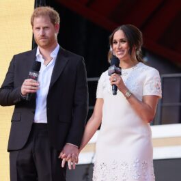 Prințul Harry și Meghan Markle la Global Citizen Live, 2021. Pe scenă, el a purtat un costum negru și o cămașă albastră. Ea a purtat o rochie albă, cu mânecă scurtă