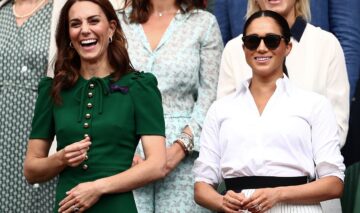Kate Middleton și Meghan Markle, tribuna regală la Turneul de la Wimbledon, 2019. Kate poartă o rochie verde, Meghan Poartă o cămașă albă și o fustă cu o fundă neagră în talie, plus ochelari de soare