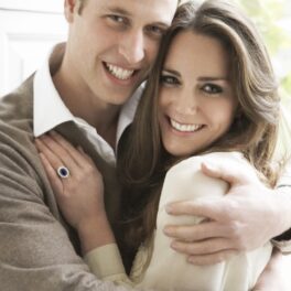 Prințul William și Kate Middleton în imaginea aniversării logodne lor din anul 2010. El poartă un pulover bej, cu o cămașă albă. Ea poartă o bluză albă și inelul de logodnă. SE țin în brațe, pe un fundal cu o fereastră
