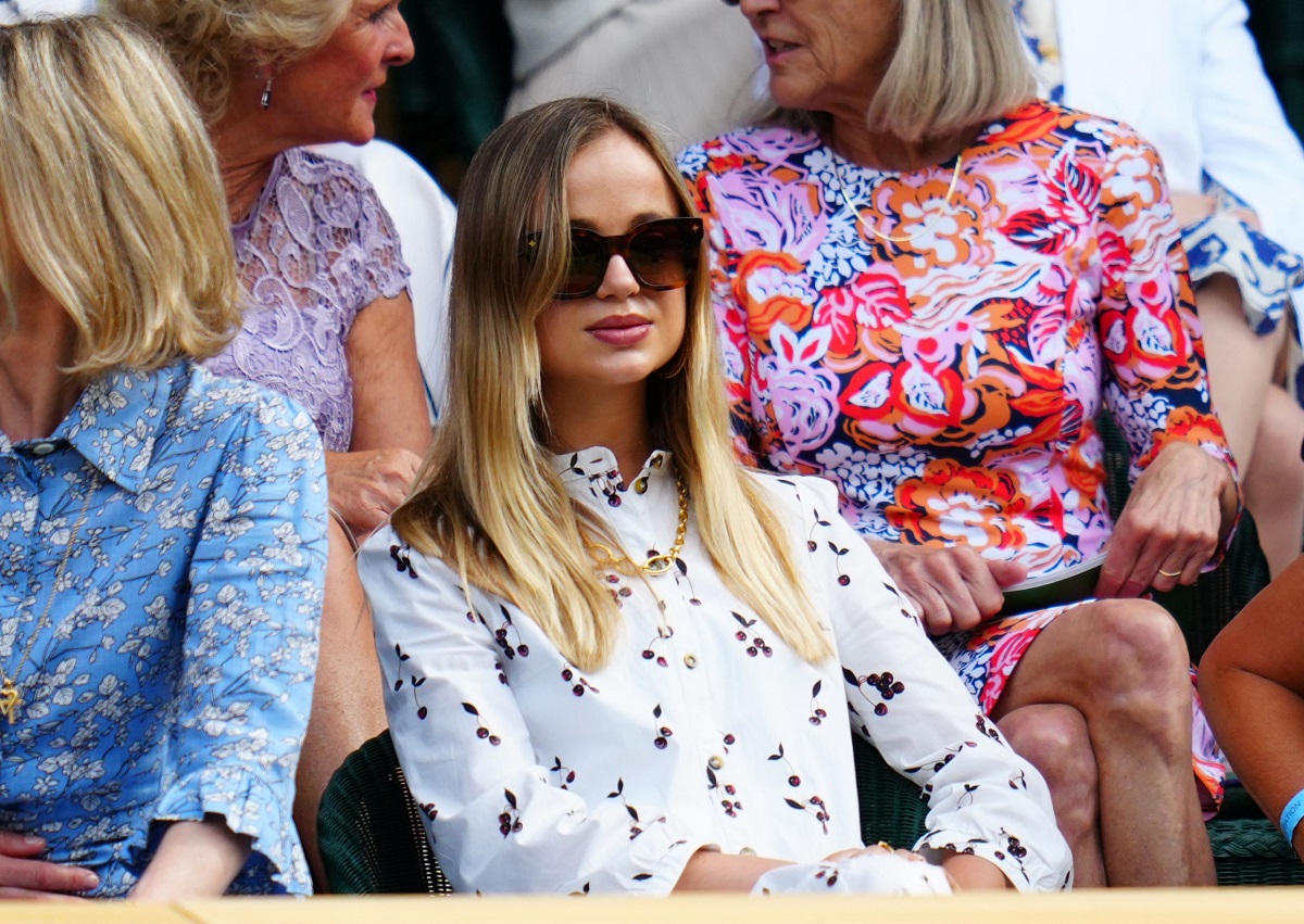 Lady Amelia Windsor la Turneul Wimbledon din anul 2019. Poartă o cămașă albă, cu imprimeu colorat și ochelari de soare. Are părul blond și lung