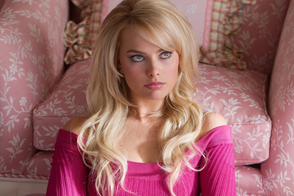 Margot Robbie în filmul The Wolf of Wall Street. E îmbrăcată în roz, blondă și are pe fundal mobilă cu roz