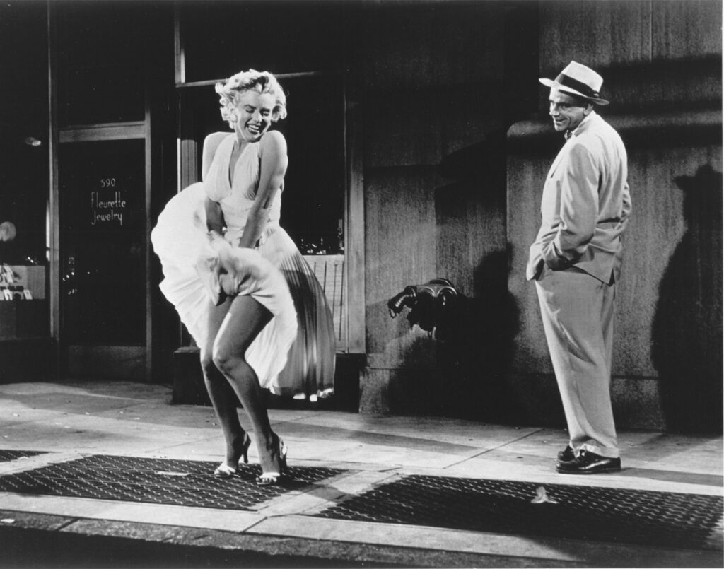 Marilyn Monroe în filmul The Seven Year Itch. Fotografie alb-negru. Poartă celebra rochie albă care se ridică