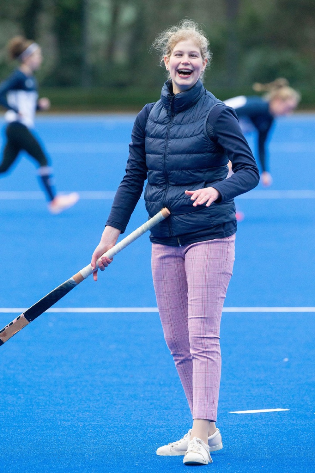 Lady Louise Windsor într-o vestă albastră și o pereche de pantaloni roz în timp ce joacă hockey