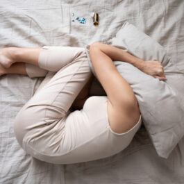 O femeie care stă cu genunchii la gură, cu perna pe cap, din cauza durerilor din timpul menopauzei