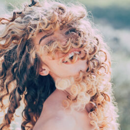 O femeie cu părul creț, cu buclele pe față, în natură