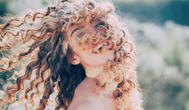 O femeie cu părul creț, cu buclele pe față, în natură