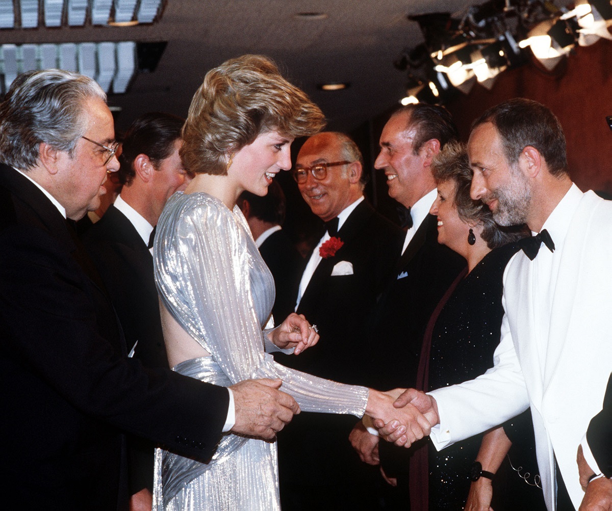 Prințesa Diana la premiera A view to a kill, din 1985. Poartă o rochie albastră, cu umerii mari, și dă mâna cu un tip îmbrăcat în alb