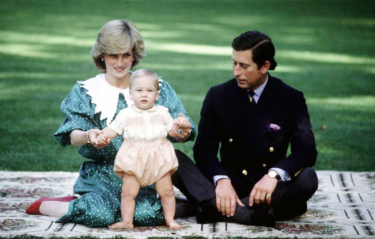 Diana, prințul Charles și Prințul William în turul oficial din Australia și Noua Zeelandă, în anul 1983. Diana poartă o rochie verde, cu guler alb, William e îmbrăcat în galben și Prințul Charles poartă un costum negru. Fundal cu verdeață