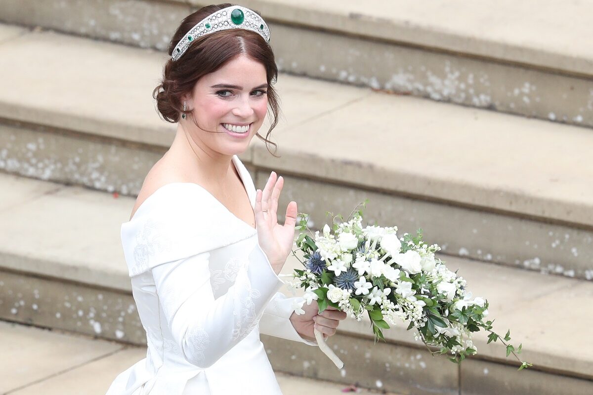 Prințesa Eugenie la nunta ei din 2018. E îmbrăcată în alb și poartă un buchet de flori albe în mână. Pe fundal scări