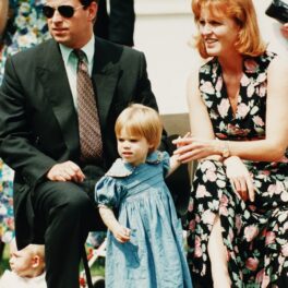 Prințul Andrew, Sarah Ferguson, Prințesa Eugenie la un eveniment oficial, pe iarbă. Sarah poartă o rochie neagră, cu motive florale, Andrew oartă costum și cravată și Eugenie poartă o rochie albastră