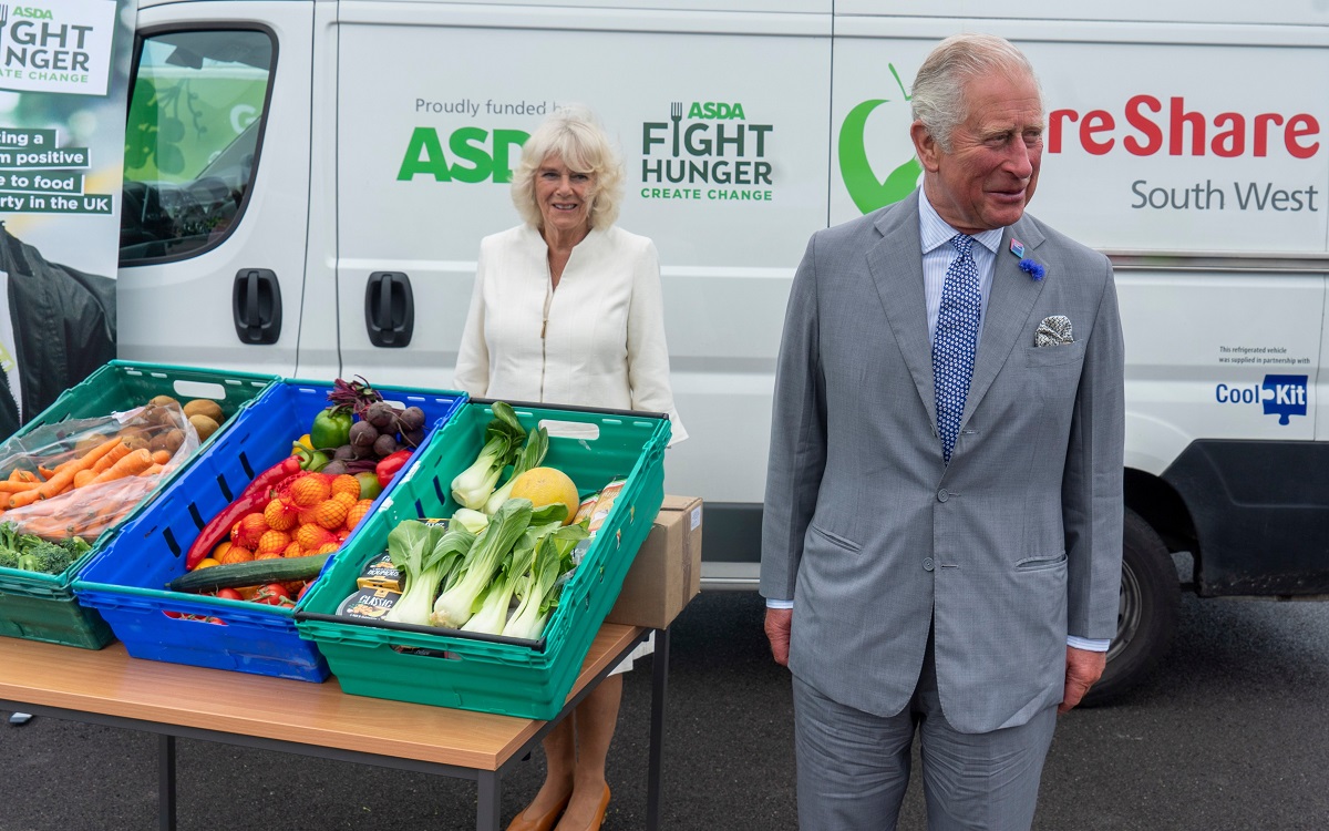 Prințul Charles și Camilla la un eveniment dedicat alimentelor, în Bristol, 2020. Ea poartă un costum alb și are lăzi cu legume în față, el are un costum gri