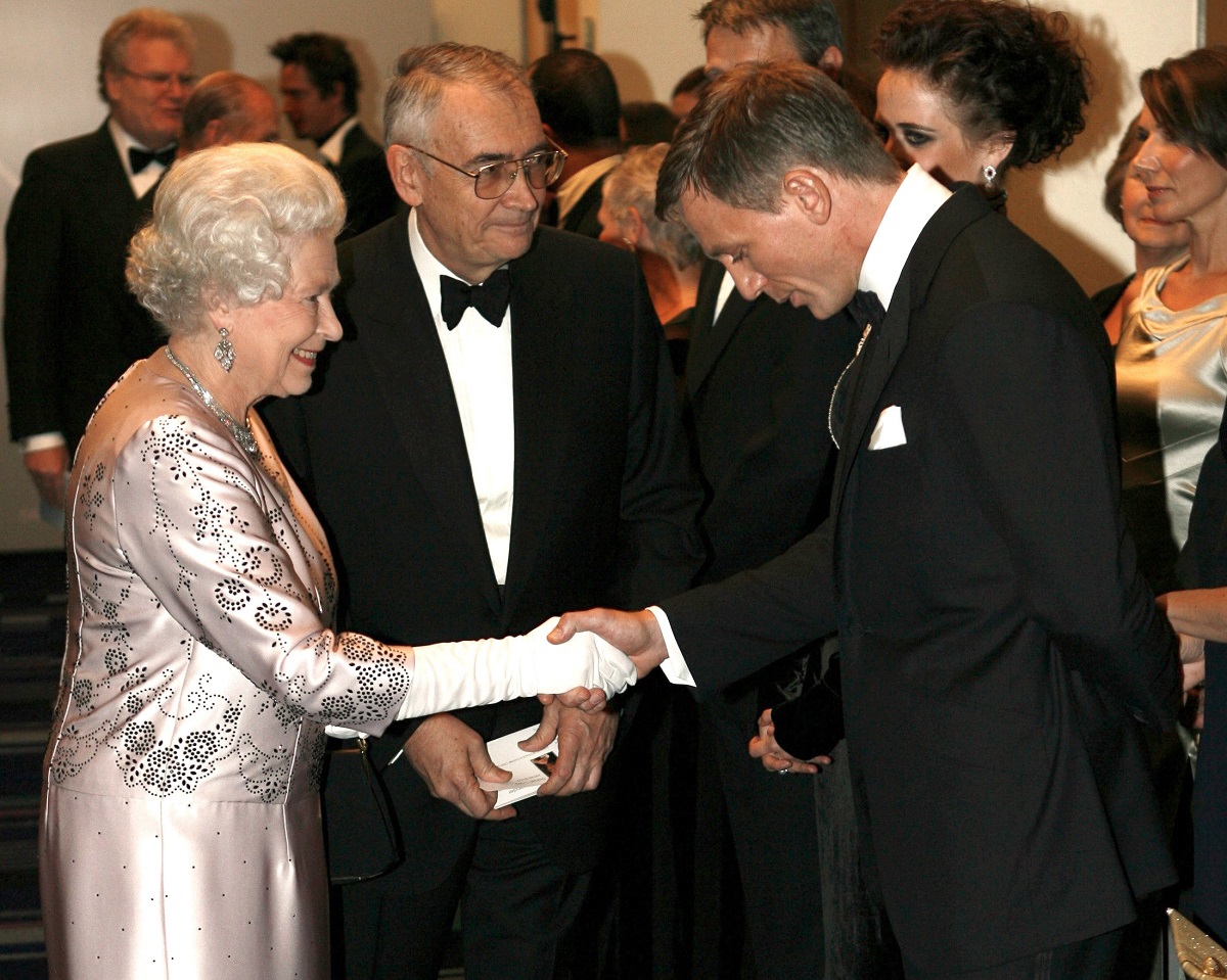 Regina Elisabeta și Daniel Craig, în 2006, la premiera Casino Royale, din Londra. Ea poartă o ținută mov deschis, cu motive argintii. El poartă un costum negru