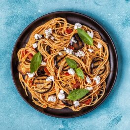 Spaghetti alla Norma într-o farfurie neagră care este așezată pe un blat albastru
