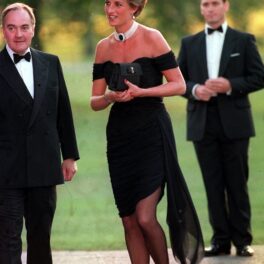 Prințesa Diana, în 1994, când purta revenge dress, rochia răzbunării. Rochia e neagră, ea poartă un colier cu perle, are părul scurt și blond. Doi bărbați pe fundal
