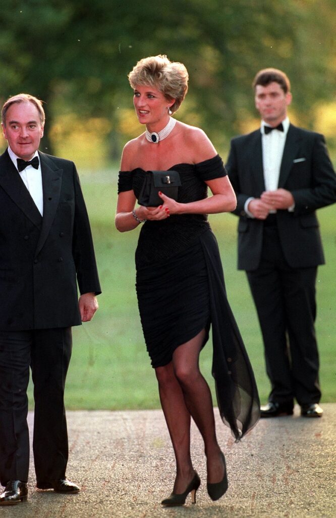 Prințesa Diana, în 1994, când purta „revenge dress”, „rochia răzbunării”. Rochia e neagră, ea poartă un colier cu perle, are părul scurt și blond. Doi bărbați pe fundal