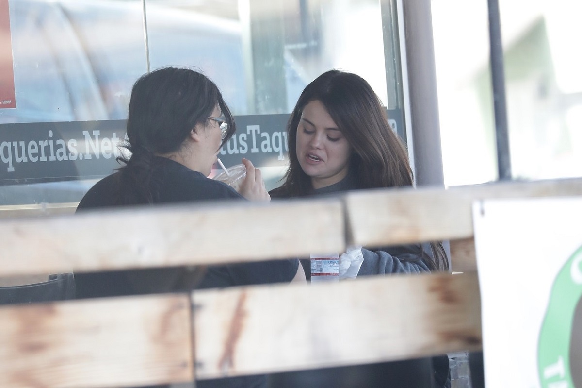 Selena Gomez mănâncă un prânz cu o prietenă. E îmrăcată cu o bluză gri. Prirtena poartă bluză neagră