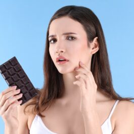 O femeie frumoasă care ține în mână ciocolată, fiind unul dintre acele alimente care cauzează apariția acneei